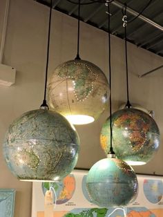 three globes hanging from the ceiling in a room with maps on it and lights above them