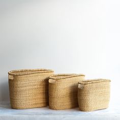 three woven baskets sitting next to each other on a white tablecloth covered surface, with one empty basket in the middle