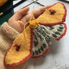 a hand holding a knitted butterfly on top of a piece of paper