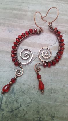 a pair of red glass beads and silver wire on a marble counter top with earrings hanging from them