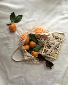 two oranges in a mesh bag on a white sheet next to an open book