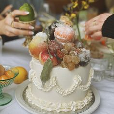 two people are decorating a white cake with fruit on the top and frosting