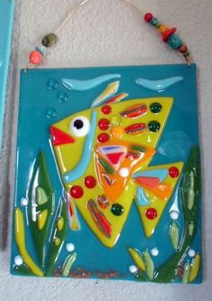 a colorful glass fish hanging on the wall next to a beaded necklace and bracelet