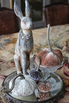 a rabbit figurine sitting on top of a plate with pumpkins and gourds