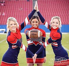 three cheerleaders in red and blue outfits are holding a football on the field