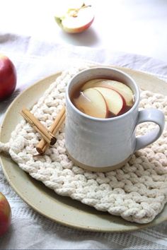 a cup of tea with cinnamon and apple slices on a white plate next to some apples