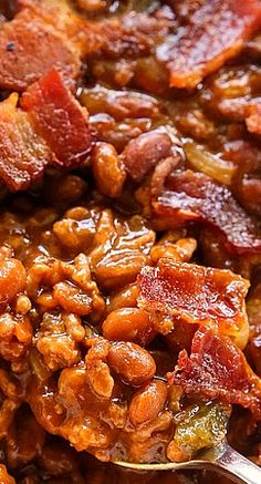 a spoon full of beans and bacon on top of a bowl with other food in it