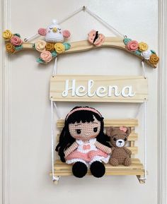 a crocheted doll and teddy bear on a wooden sign hanging from a door