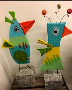 two colorful bird sculptures sitting on top of stone block stands in front of a white wall
