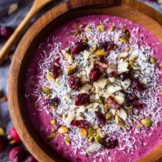 a wooden bowl filled with smoothie topped with nuts and cranberry toppings