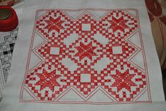a red and white cross stitched design on a table cloth next to a spool of thread