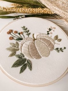 an embroidered pumpkin with leaves and flowers on a white surface next to some wheat stalks