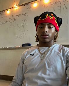 a young man with dreadlocks and a red bandana sits in front of a whiteboard