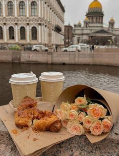 two cups of coffee and pastries on a table next to the water with flowers