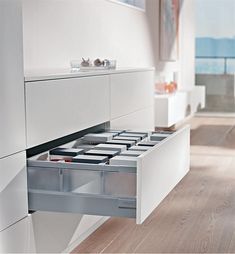 an open drawer in a white kitchen next to a table with drawers on the side