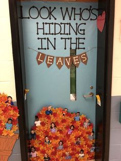 a door decorated with orange flowers and paper cutouts that read, look who's hiding in the leaves