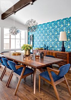 a dining room table with blue chairs in front of a large wallpapered background