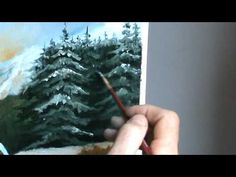 someone is holding a pencil and painting a snowy scene with pine trees in the background