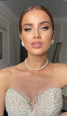 a woman in a wedding dress with pearls on her necklace and earrings, looking at the camera