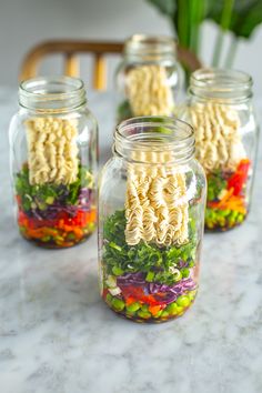 four mason jars filled with noodles and vegetables