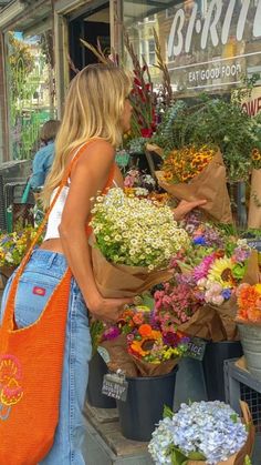 a woman standing in front of a flower shop with lots of colorful flowers on display