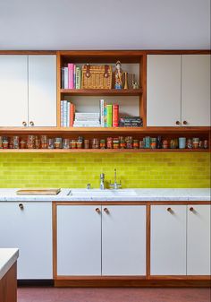 a kitchen with white cabinets and yellow tile backsplash, wooden shelves above the sink