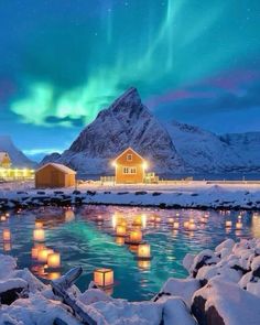some lights floating in the water next to a mountain and snow covered ground with houses
