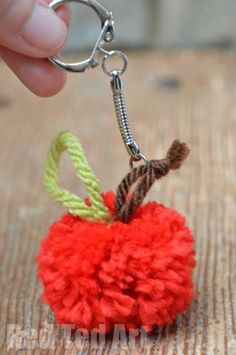 a hand holding a red pom - pom keychain on top of a wooden table