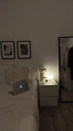 a laptop computer sitting on top of a bed next to a night stand and mirror