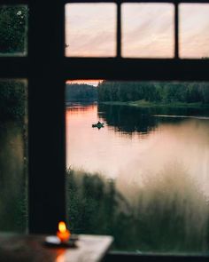 a candle is lit in front of a window with a view of the water and trees