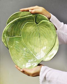 two hands holding a large green leaf shaped plate