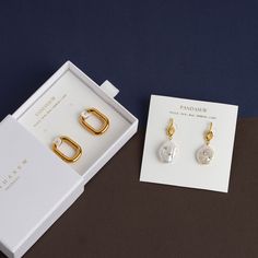 two pairs of earrings sitting on top of a table next to a card and box