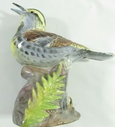 a ceramic bird sitting on top of a green plant