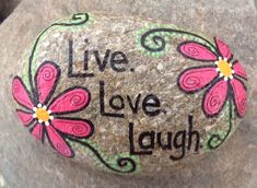 a painted rock that says live, love, laugh with flowers and swirls on it