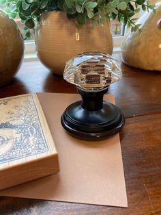 a glass object sitting on top of a wooden table next to a book and plant