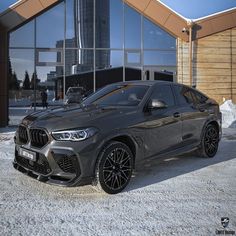 a grey bmw suv parked in front of a building with large windows and snow on the ground