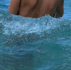 a man swimming in the ocean with his back turned to the camera and no shirt on