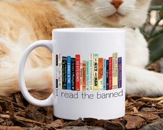 a cat laying on the ground next to a coffee mug that says i read the banned