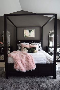 a black and white bedroom with pink fur rugs on the floor, four poster bed