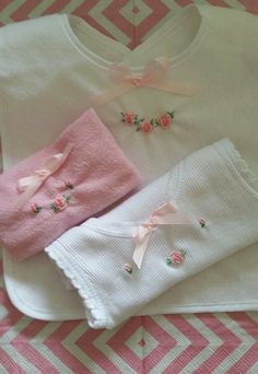 three baby clothes laying on top of a pink and white blanket