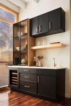 a kitchen with black cabinets and wooden flooring next to a window overlooking the water