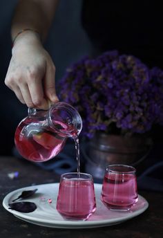 a person pouring pink liquid into glasses on a plate