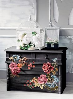an old dresser with flowers painted on it and a birdcage in the background