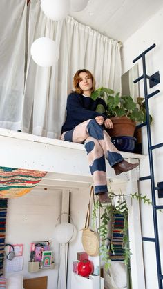 a woman sitting on top of a loft bed next to a plant in a pot