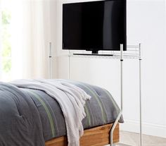 a flat screen tv sitting on top of a metal stand next to a bed in a bedroom