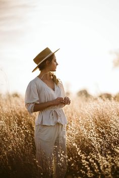 a woman standing in tall grass wearing a hat