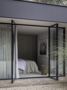 a bedroom with glass walls and sliding doors leading to the bed area is seen from outside