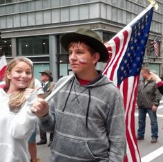 a man and woman holding an american flag in the street with other people standing around