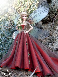 a doll dressed as a fairy holding a flower in her hand and standing next to a tree