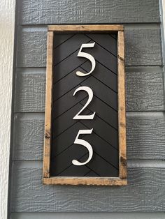 a house number sign mounted to the side of a gray wooden building with white numbers on it
